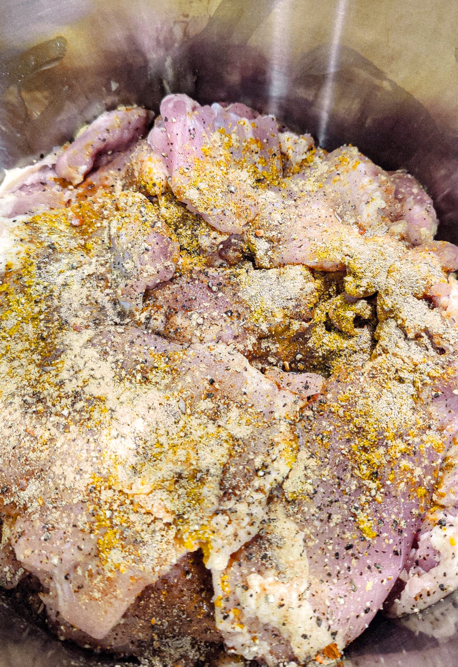 Aerial view of all the chicken added to the pot, with more seasonings on top.