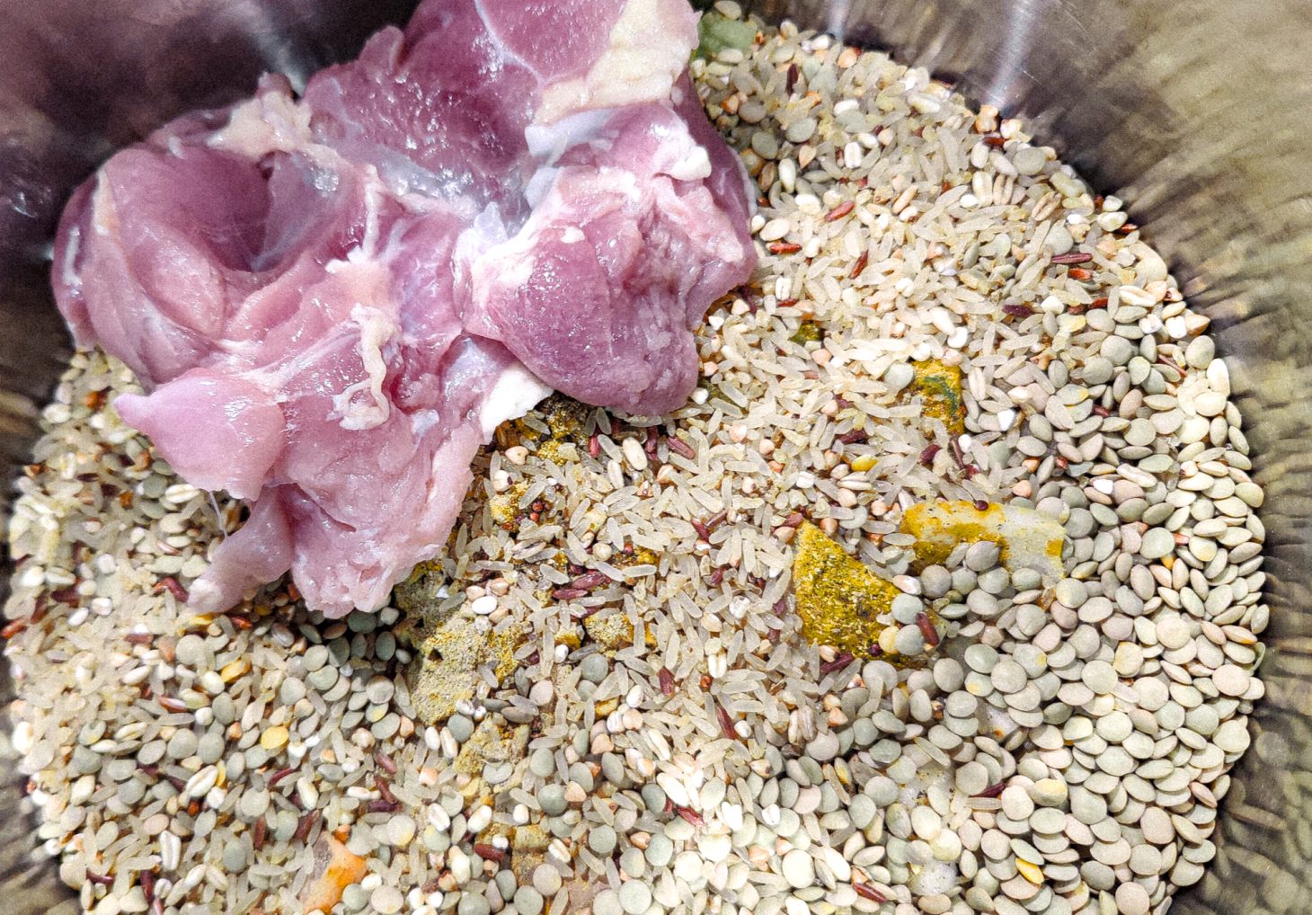 Aerial view of pot with grains, seasonings and the first piece of chicken laid over it all.